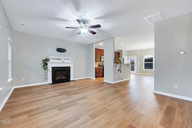 unfurnished living room featuring ceiling fan with notable chandelier and light wood-type flooring