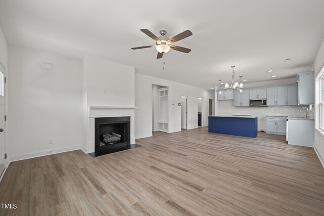 unfurnished living room with sink, ceiling fan with notable chandelier, and light hardwood / wood-style floors