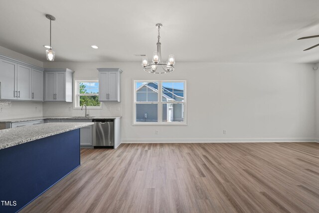 kitchen with ceiling fan with notable chandelier, light hardwood / wood-style flooring, decorative light fixtures, dishwasher, and light stone countertops