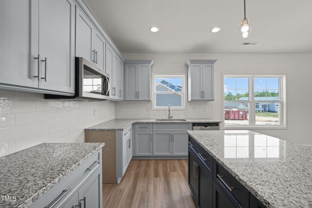 kitchen featuring light hardwood / wood-style flooring, appliances with stainless steel finishes, light stone countertops, sink, and decorative backsplash