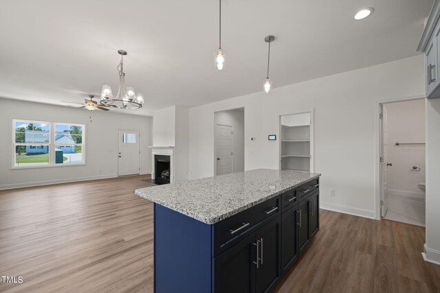 kitchen with ceiling fan with notable chandelier, pendant lighting, light hardwood / wood-style flooring, a center island, and light stone counters