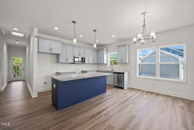 kitchen featuring light wood-type flooring, pendant lighting, stainless steel appliances, and light stone countertops