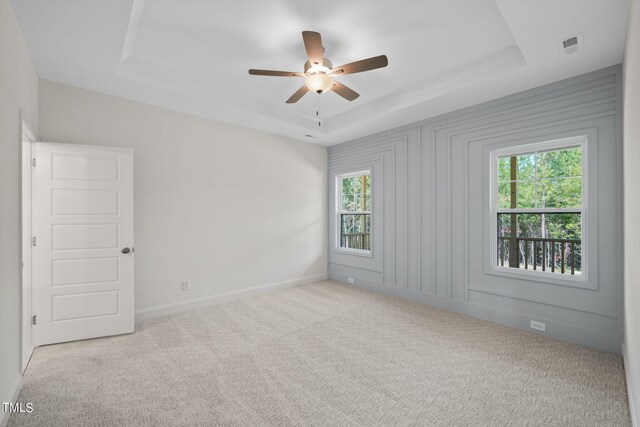 unfurnished room featuring a raised ceiling, light colored carpet, and ceiling fan