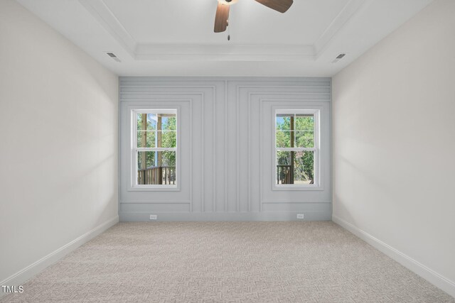 empty room with a raised ceiling, ceiling fan, and light carpet