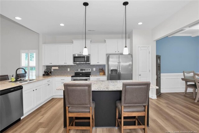 kitchen with light hardwood / wood-style flooring, a kitchen bar, stainless steel appliances, sink, and white cabinets