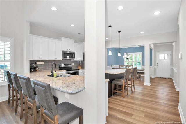 kitchen with pendant lighting, appliances with stainless steel finishes, light hardwood / wood-style floors, a kitchen bar, and white cabinetry