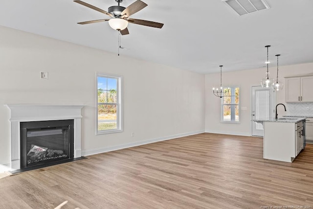 unfurnished living room featuring ceiling fan with notable chandelier, light hardwood / wood-style flooring, and sink