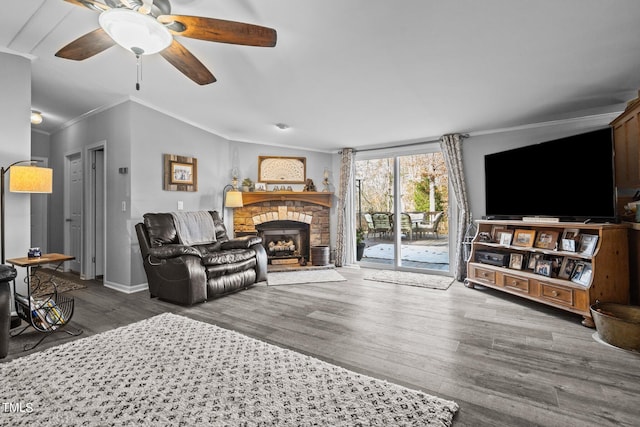 living room with crown molding, dark wood-type flooring, ceiling fan, and a stone fireplace