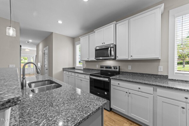 kitchen featuring white cabinetry, sink, hanging light fixtures, stainless steel appliances, and light wood-type flooring