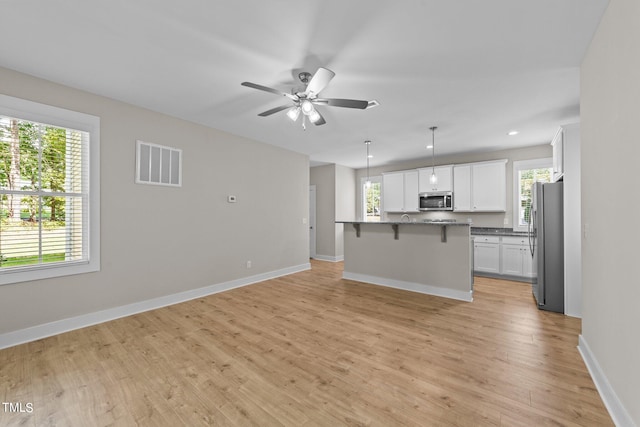 kitchen with a breakfast bar, appliances with stainless steel finishes, white cabinetry, and a wealth of natural light