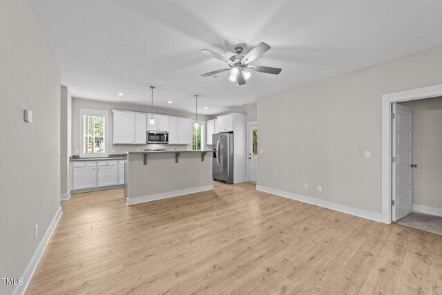 kitchen with a center island, white cabinets, hanging light fixtures, light wood-type flooring, and appliances with stainless steel finishes