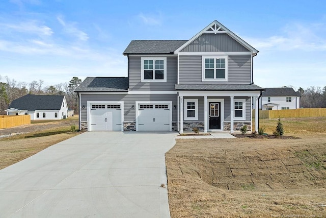 craftsman-style house with driveway, stone siding, covered porch, fence, and board and batten siding