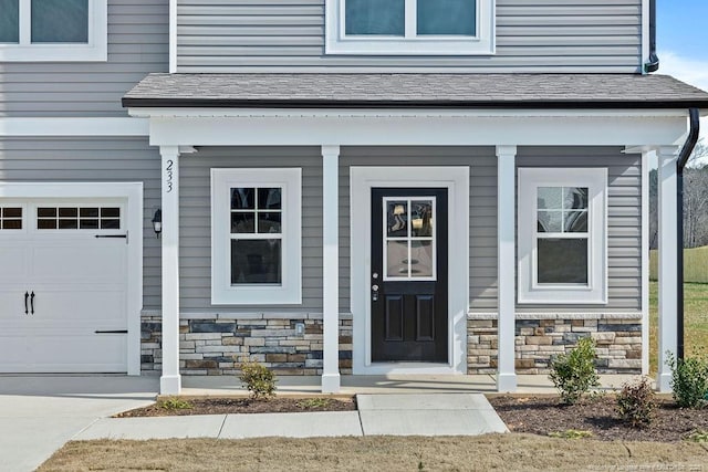 doorway to property featuring a garage, stone siding, and roof with shingles