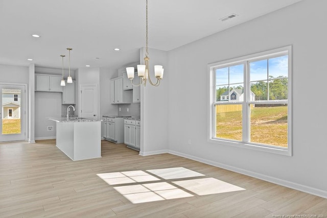 kitchen with light stone counters, a notable chandelier, a sink, and light wood finished floors