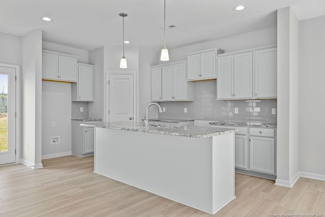 kitchen featuring visible vents, light wood finished floors, a center island with sink, and decorative backsplash