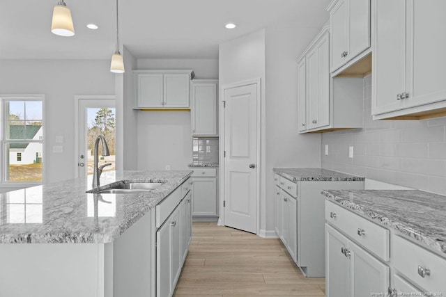 kitchen featuring light wood-style flooring, a sink, white cabinetry, light stone countertops, and decorative light fixtures