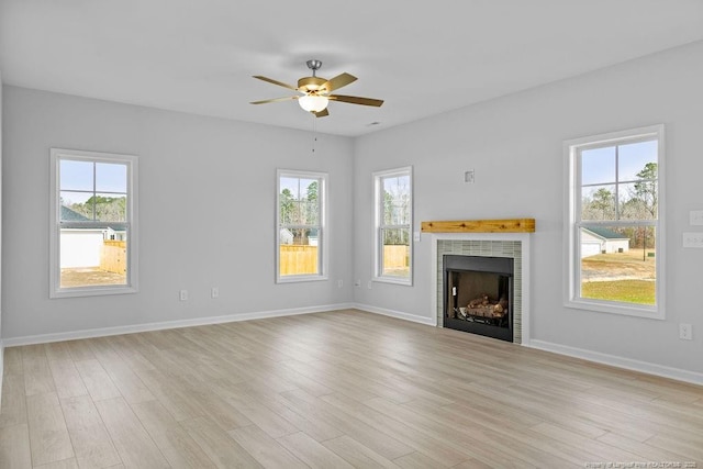 unfurnished living room featuring a tiled fireplace, light wood finished floors, plenty of natural light, and baseboards