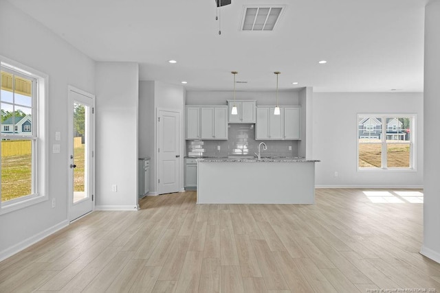 kitchen with light wood finished floors, backsplash, a sink, and visible vents