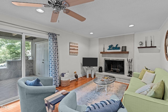 living room featuring ornamental molding, a textured ceiling, a brick fireplace, ceiling fan, and hardwood / wood-style flooring