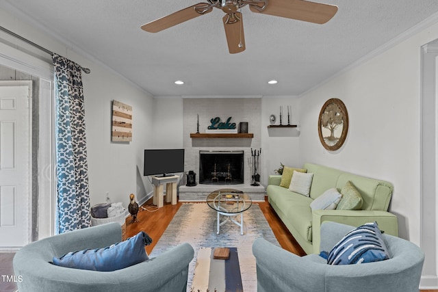 living room with a fireplace, hardwood / wood-style floors, ceiling fan, ornamental molding, and a textured ceiling