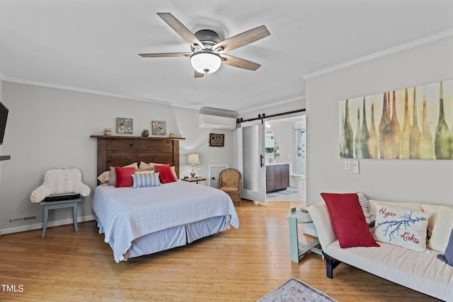 bedroom with a wall unit AC, ensuite bath, ceiling fan, a barn door, and light hardwood / wood-style floors