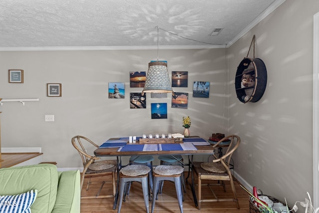 dining space with a textured ceiling, ornamental molding, and wood-type flooring