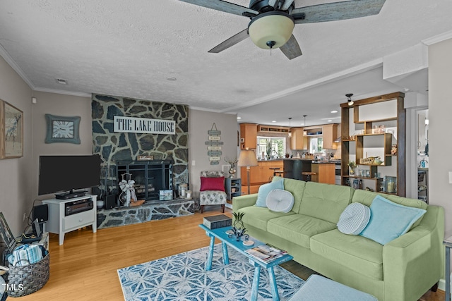 living room with a textured ceiling, light hardwood / wood-style flooring, ceiling fan, and a stone fireplace