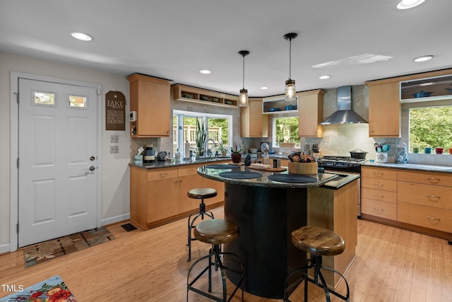 kitchen featuring gas range, a center island, a breakfast bar, wall chimney range hood, and light wood-type flooring