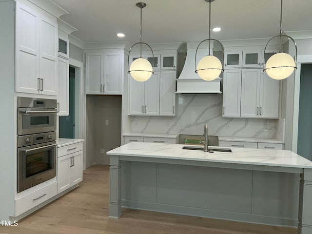 kitchen featuring white cabinets, a center island with sink, light stone counters, and sink