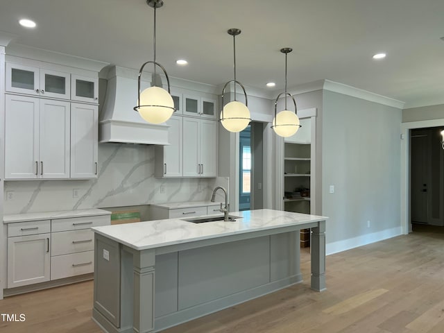 kitchen with light stone counters, a kitchen island with sink, sink, white cabinetry, and hanging light fixtures