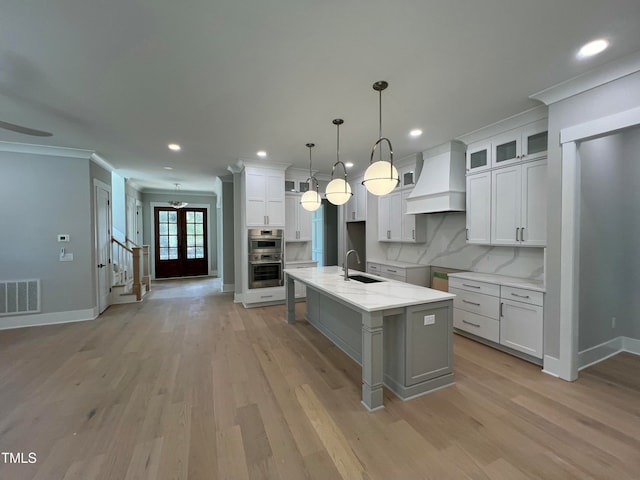 kitchen with premium range hood, a kitchen island with sink, sink, decorative backsplash, and white cabinetry