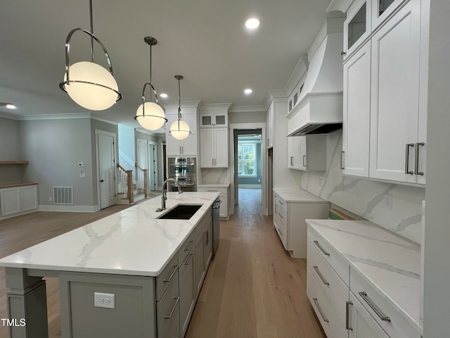 kitchen featuring backsplash, white cabinetry, a center island with sink, and premium range hood