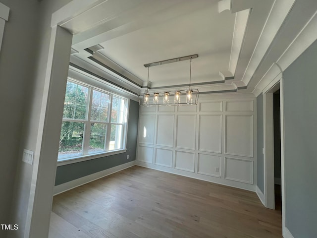 unfurnished dining area with hardwood / wood-style floors, a raised ceiling, crown molding, and a notable chandelier