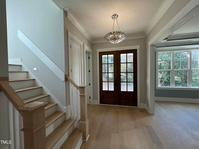 entrance foyer with ornamental molding, french doors, a chandelier, and light wood-type flooring