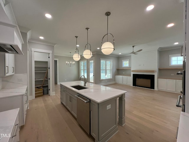 kitchen featuring dishwasher, a center island with sink, sink, hanging light fixtures, and light stone counters