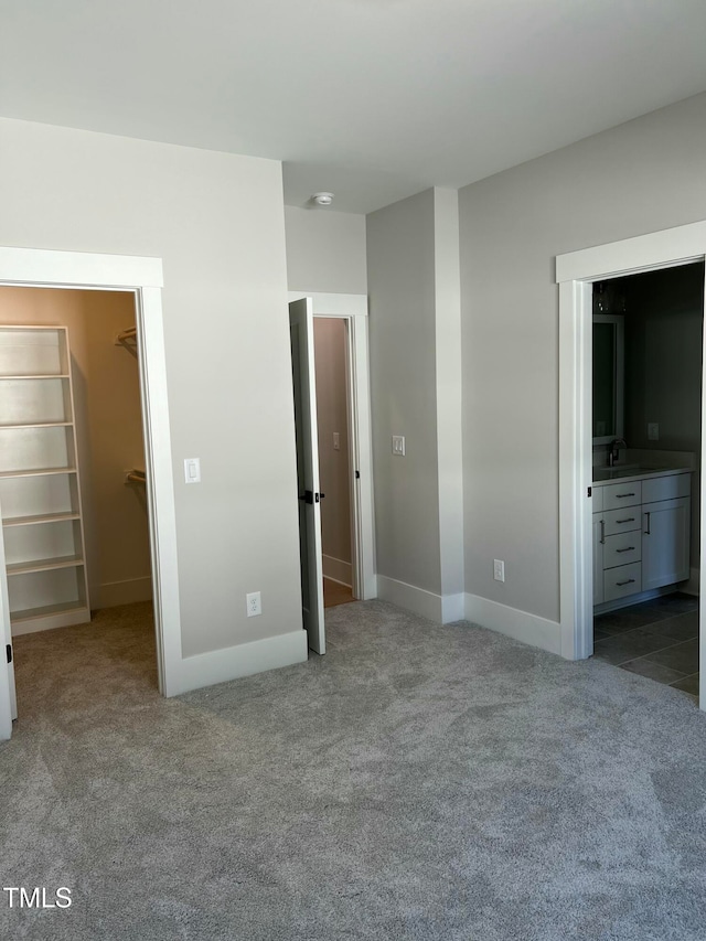 unfurnished bedroom featuring light carpet, a walk in closet, sink, connected bathroom, and a closet