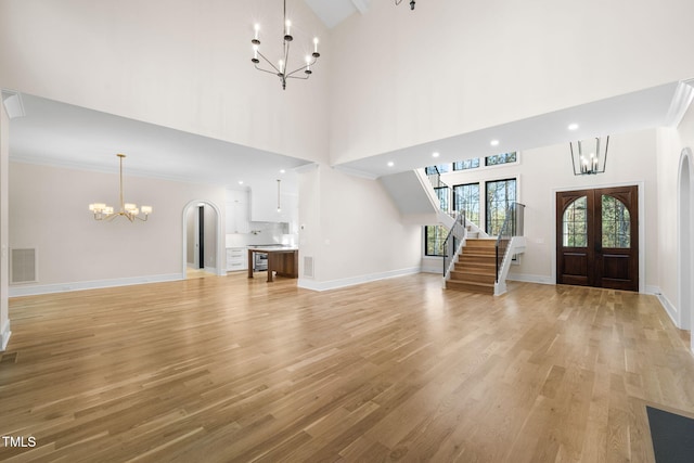 unfurnished living room with french doors, ornamental molding, high vaulted ceiling, light hardwood / wood-style flooring, and a notable chandelier