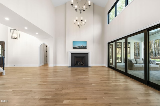 unfurnished living room featuring a notable chandelier, light hardwood / wood-style floors, high vaulted ceiling, and french doors