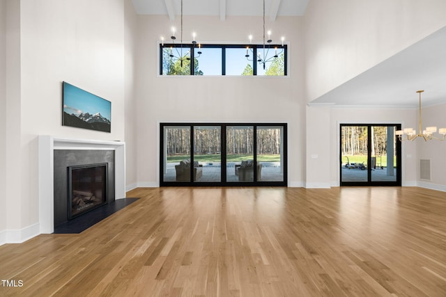 unfurnished living room with crown molding, a towering ceiling, a chandelier, and hardwood / wood-style flooring