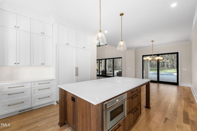 kitchen with white cabinets, a center island, decorative light fixtures, and light hardwood / wood-style flooring