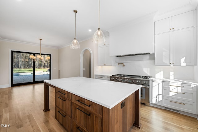 kitchen with stainless steel range, decorative light fixtures, white cabinets, light hardwood / wood-style floors, and a kitchen island