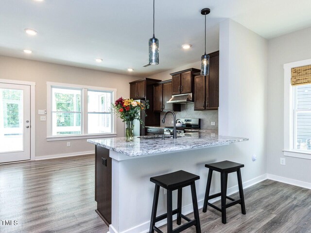 kitchen with light stone countertops, kitchen peninsula, tasteful backsplash, hanging light fixtures, and stainless steel electric range