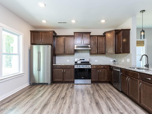 kitchen featuring hanging light fixtures, sink, light wood-type flooring, appliances with stainless steel finishes, and light stone counters