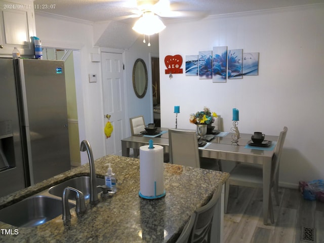 kitchen with light hardwood / wood-style flooring, stainless steel fridge with ice dispenser, sink, ceiling fan, and dark stone counters