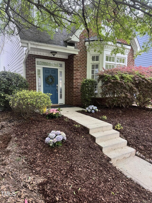 entrance to property featuring brick siding and a shingled roof