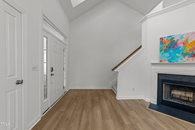 entryway featuring wood finished floors, a fireplace, vaulted ceiling, and stairway