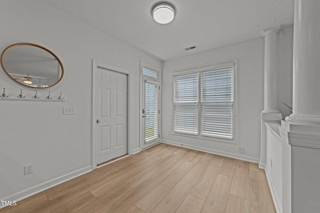 interior space with baseboards, a ceiling fan, light wood-style floors, visible vents, and decorative columns