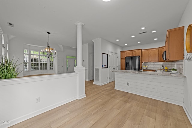 kitchen with ornate columns, a peninsula, black appliances, a chandelier, and decorative backsplash
