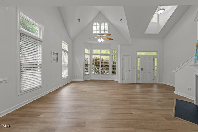 foyer entrance with baseboards, a ceiling fan, light wood finished floors, a skylight, and high vaulted ceiling