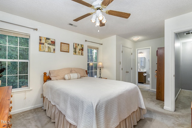 bedroom with ceiling fan, a textured ceiling, light carpet, and ensuite bath